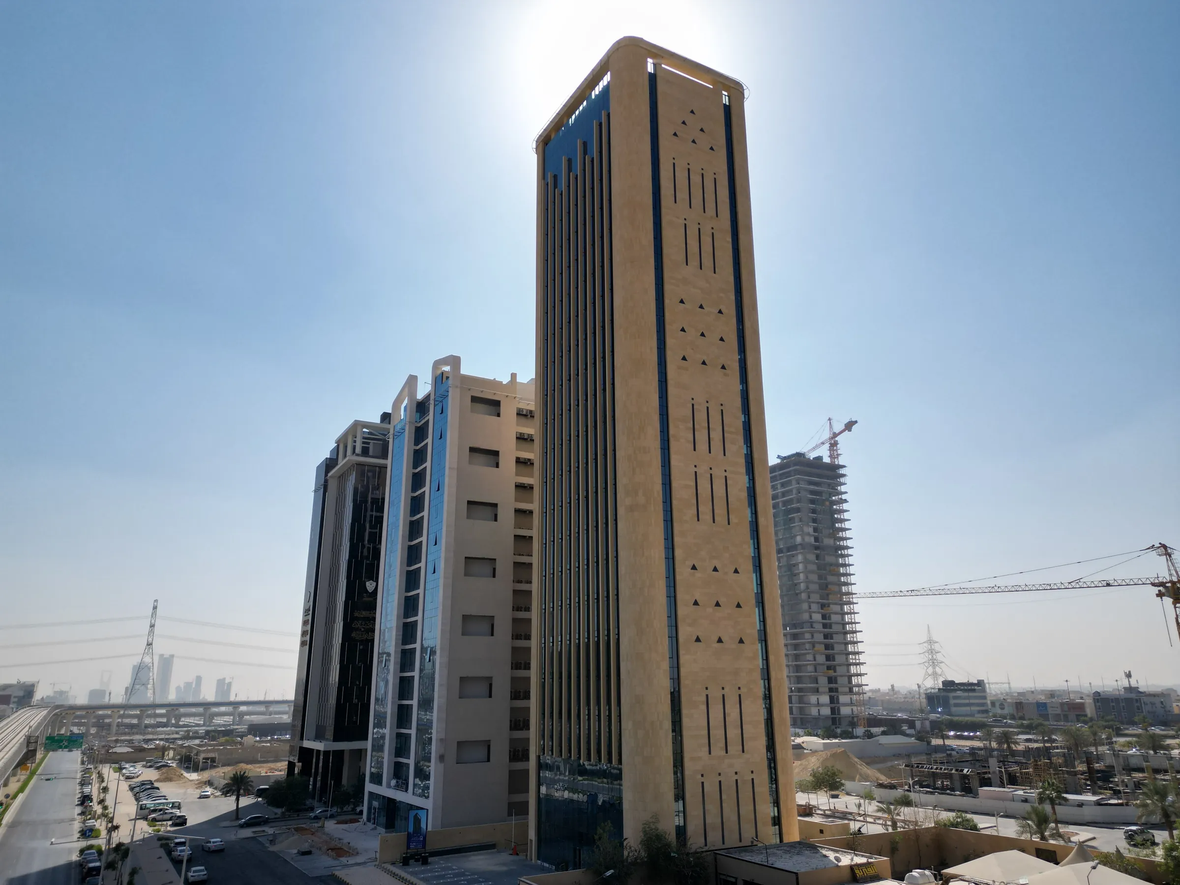 الواجهة الحجرية للبرج نهارًا، تتخللها فتحات رأسية ضيقة وزخارف مثلثة صغيرة، بجوار مبانٍ مكتبية أقل ارتفاعًا، وتظهر أبراج المركز المالي في الأفق البعيد.