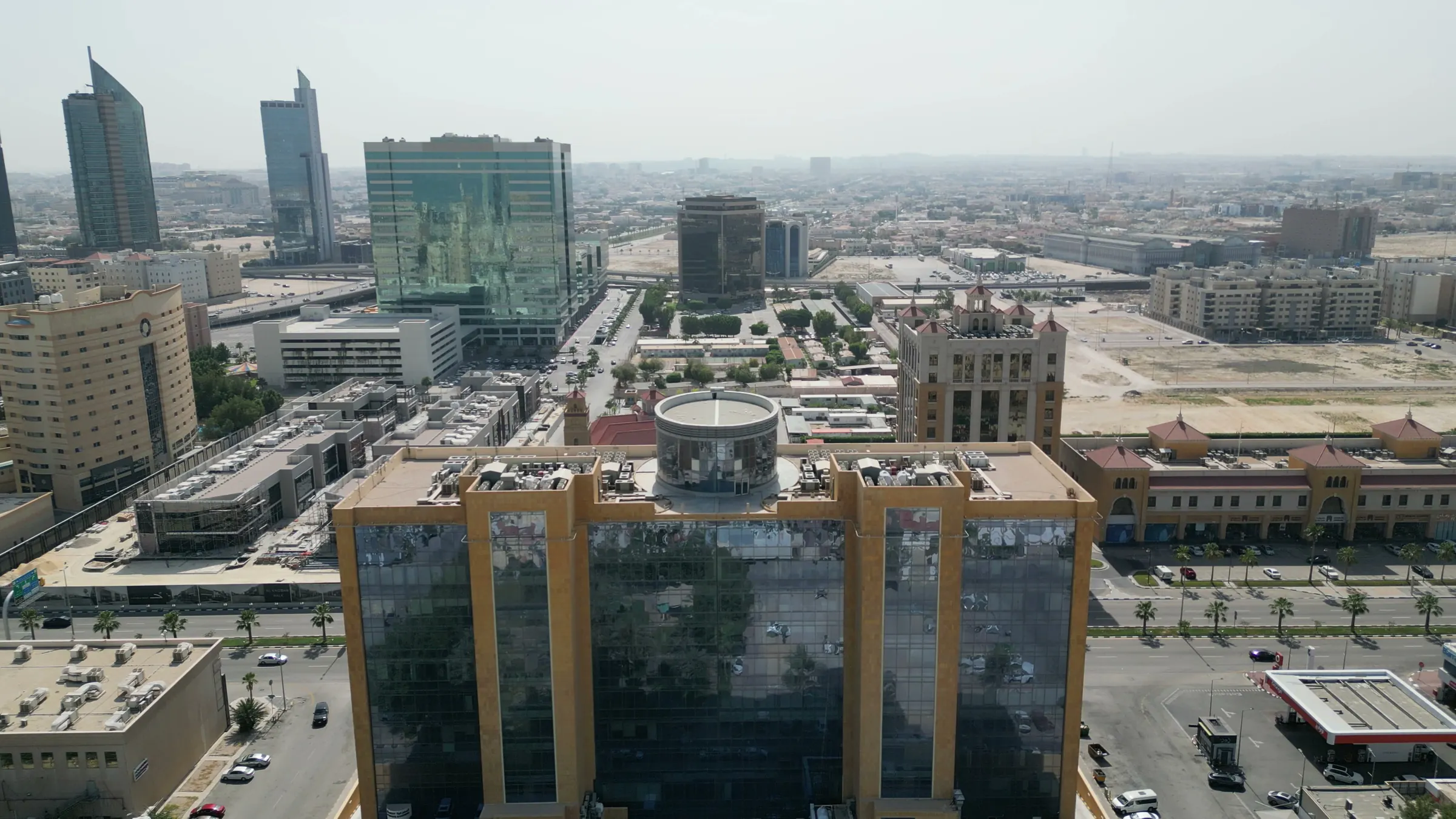 سطح البرج وأسطوانته الدائرية من الجو، وخلفه الطريق والأبراج المجاورة والمدينة ممتدة نحو الداخل.