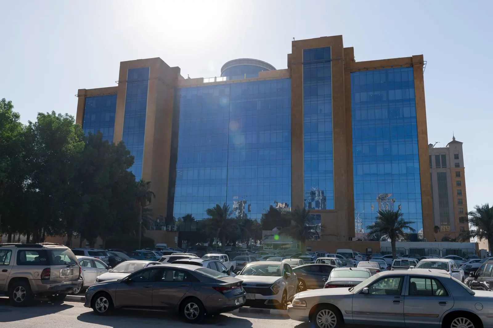 الواجهة الخلفية للبرج في مواجهة الشمس: فتحات زجاجية بين أكتاف حجرية عالية، تعلوها الأسطوانة الدائرية، وأمامها مواقف السيارات.