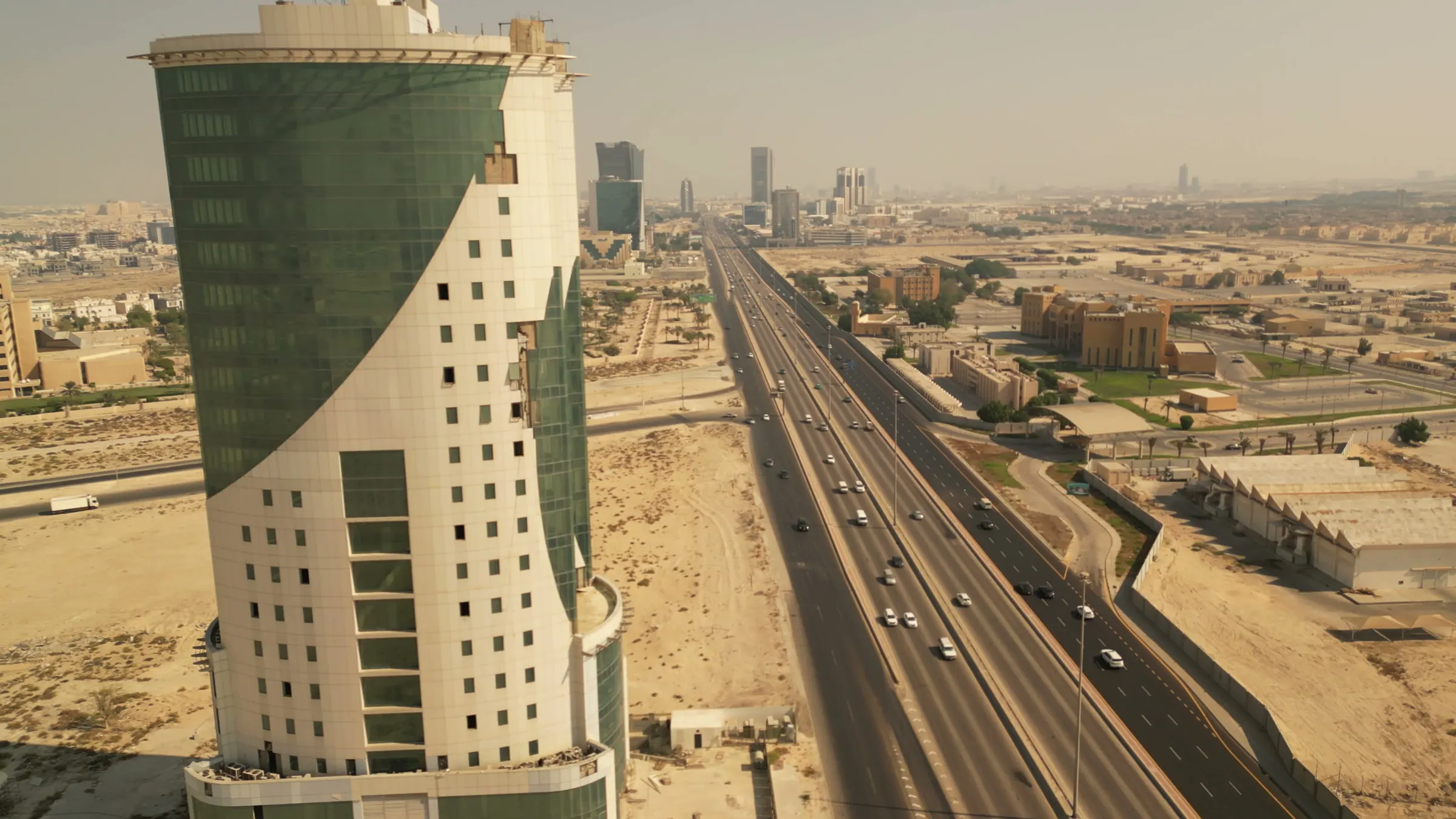 منظر جوي قريب لجانب البرج المنحني، والطريق السريع يمتد نحو أبراج المدينة في الأفق.