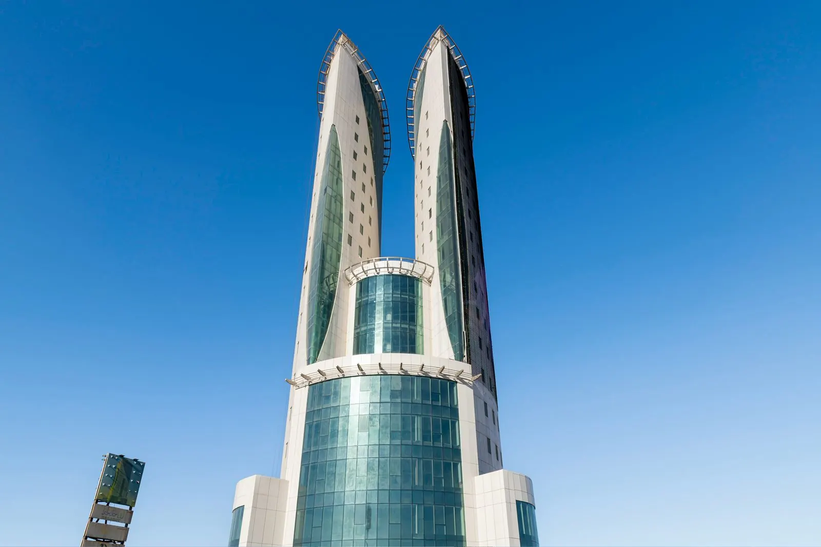 البرج من مستوى الأرض من الأمام: قاعدة زجاجية ونواة من الزجاج الأخضر بين كتلتين بيضاوين منحنيتين ترتفعان إلى قمتين.