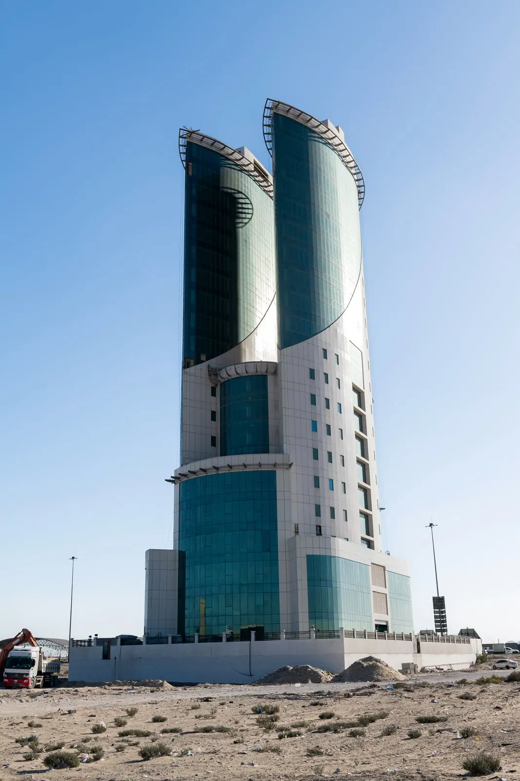 البرج من الجانب على مستوى الأرض: كتلة منحنية بيضاء وزجاج أخضر تحت سماء صافية.
