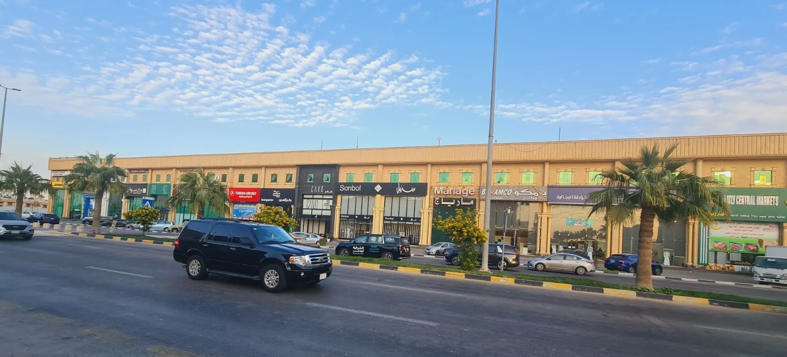 المجمع بكامل امتداده من الجهة المقابلة لطريق مزدحم، تحت سماء بغيوم متفرقة.