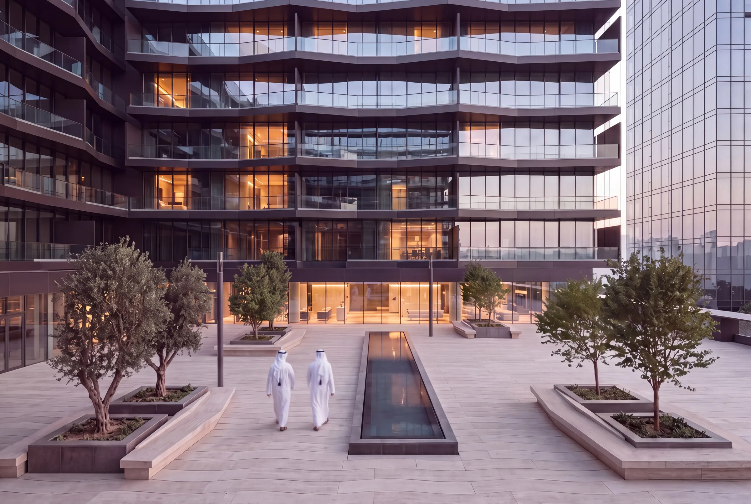 The podium deck at eye level: a paved terrace with trees, a long water channel and the main building rising behind.